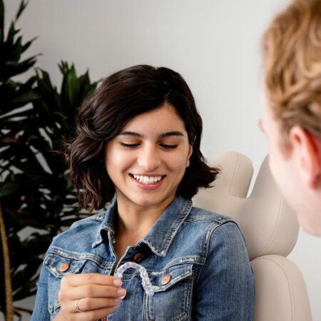 Pacjentka podczas konsultacji ortodontycznej trzyma przezroczystą nakładkę Invisalign® w gabinecie stomatologicznym.