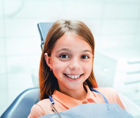 Uśmiechnięta dziewczynka na fotelu dentystycznym podczas wizyty ortodontycznej – przykład diagnostyki i planowania leczenia nakładkami Invisalign®.