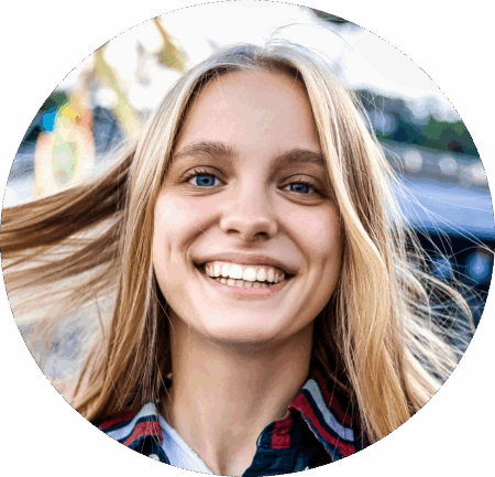 Uśmiechnięta młoda kobieta z blond włosami na zewnątrz, prezentująca zdrowe zęby – przykład efektu leczenia ortodontycznego z użyciem nakładek Invisalign®.