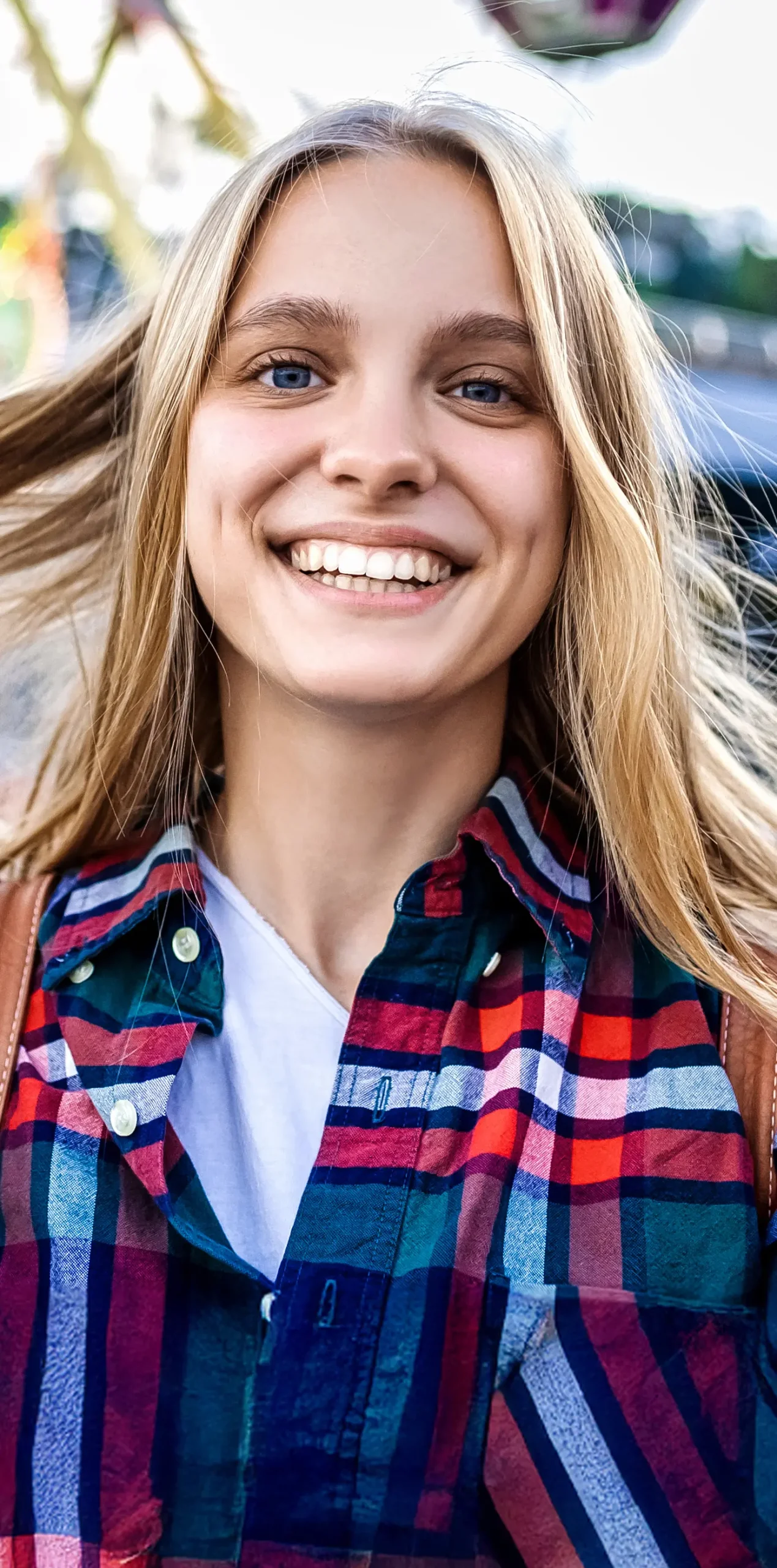 Młoda kobieta z długimi blond włosami, uśmiechająca się szeroko na zewnątrz, prezentująca zdrowe zęby – przykład naturalnego uśmiechu, istotnego w diagnostyce ortodontycznej i leczeniu nakładkami Invisalign®.