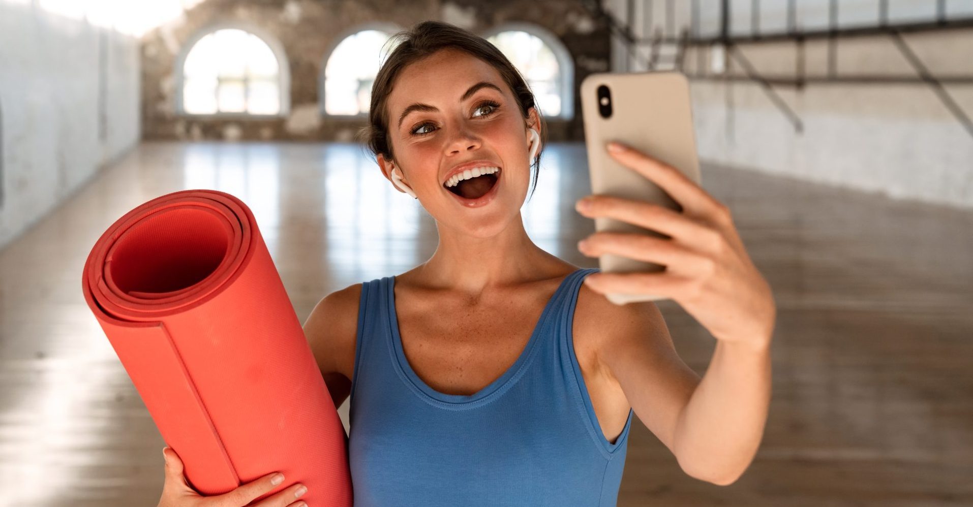 Kobieta z matą treningową, która uśmiecha się, robiąc selfie.