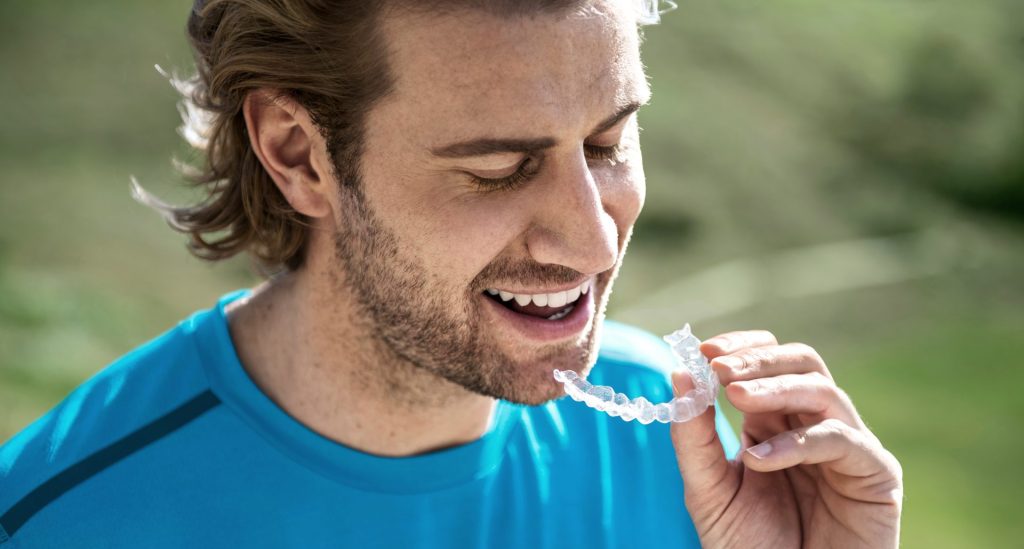 Mężczyzna w niebieskim ubraniu zakłada nakładki Invisalign.