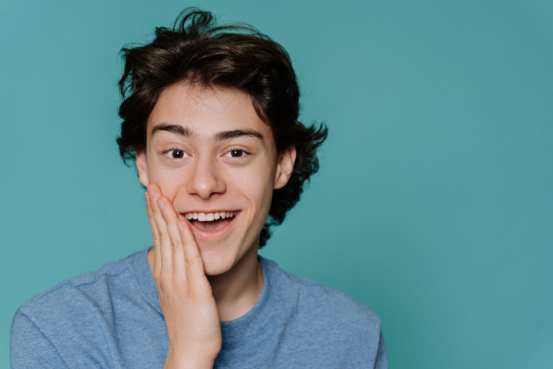 Młody mężczyzna w zielonym ubraniu trzymający dłoń przy twarzy.